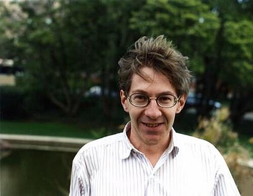 A headshot of Joseph Oesterlé, a mathematician, with a serious expression. He is bald with a white beard and glasses, wearing a suit.